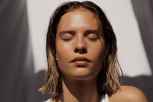 woman in sunlight with eyes closed, no makeup, clear skin