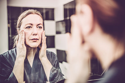 Woman looking in mirror massaging her cheeks.