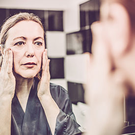 Woman looking in mirror massaging her cheeks.
