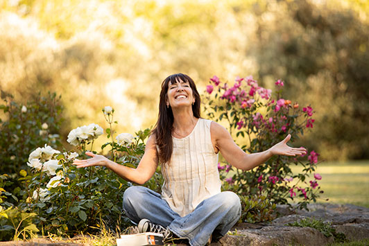 Woman smiling, sitting cross-legged on the grass with flowers looking refreshed