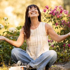 Woman smiling, sitting cross-legged on the grass with flowers looking refreshed - Thumbnail
