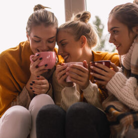 three women cozy for fall holding mugs of something warm