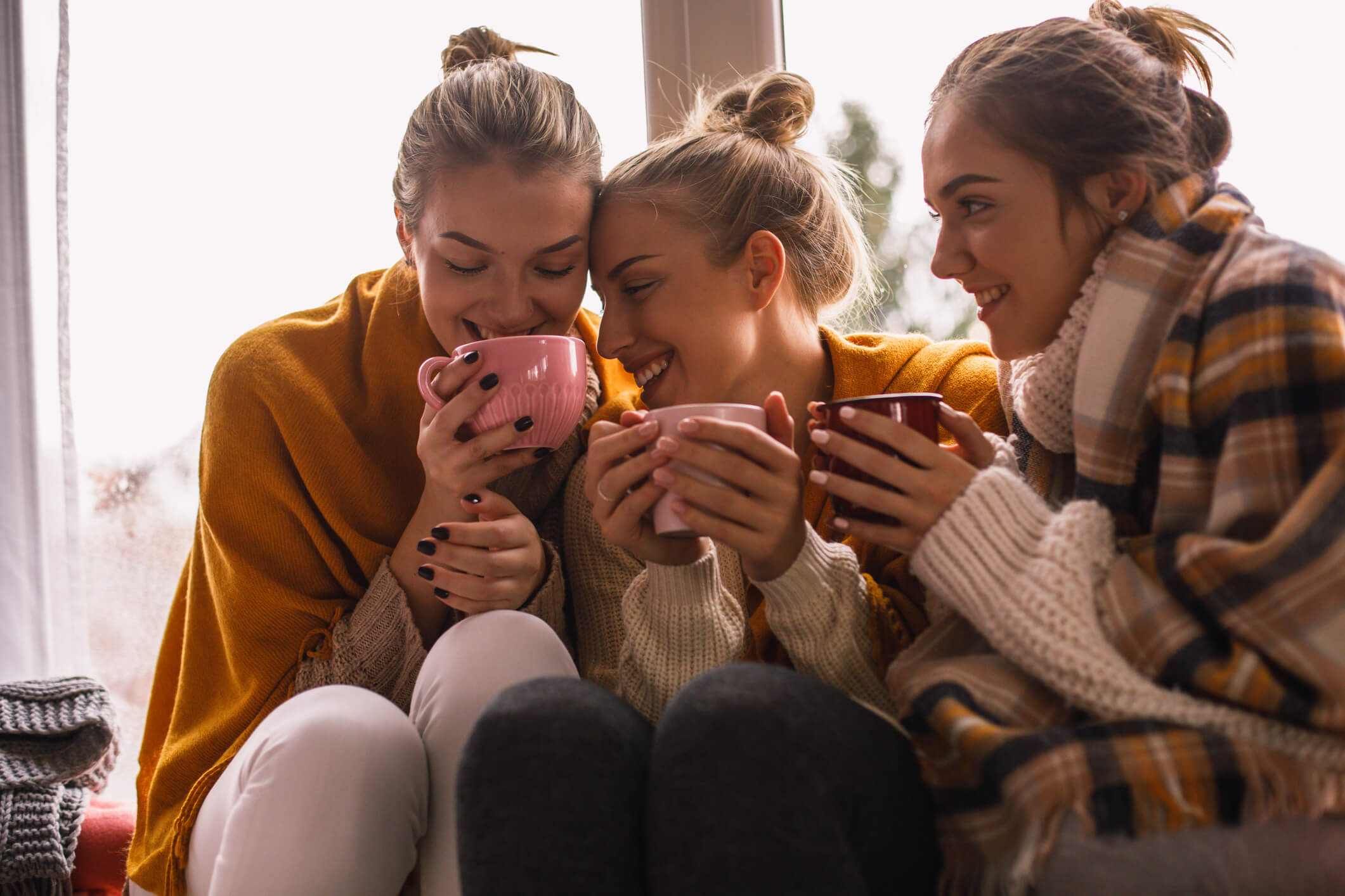 three women cozy for fall holding mugs of something warm